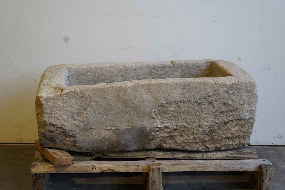 Antique stone trough planter displayed outdoors with light shadows and natural wear