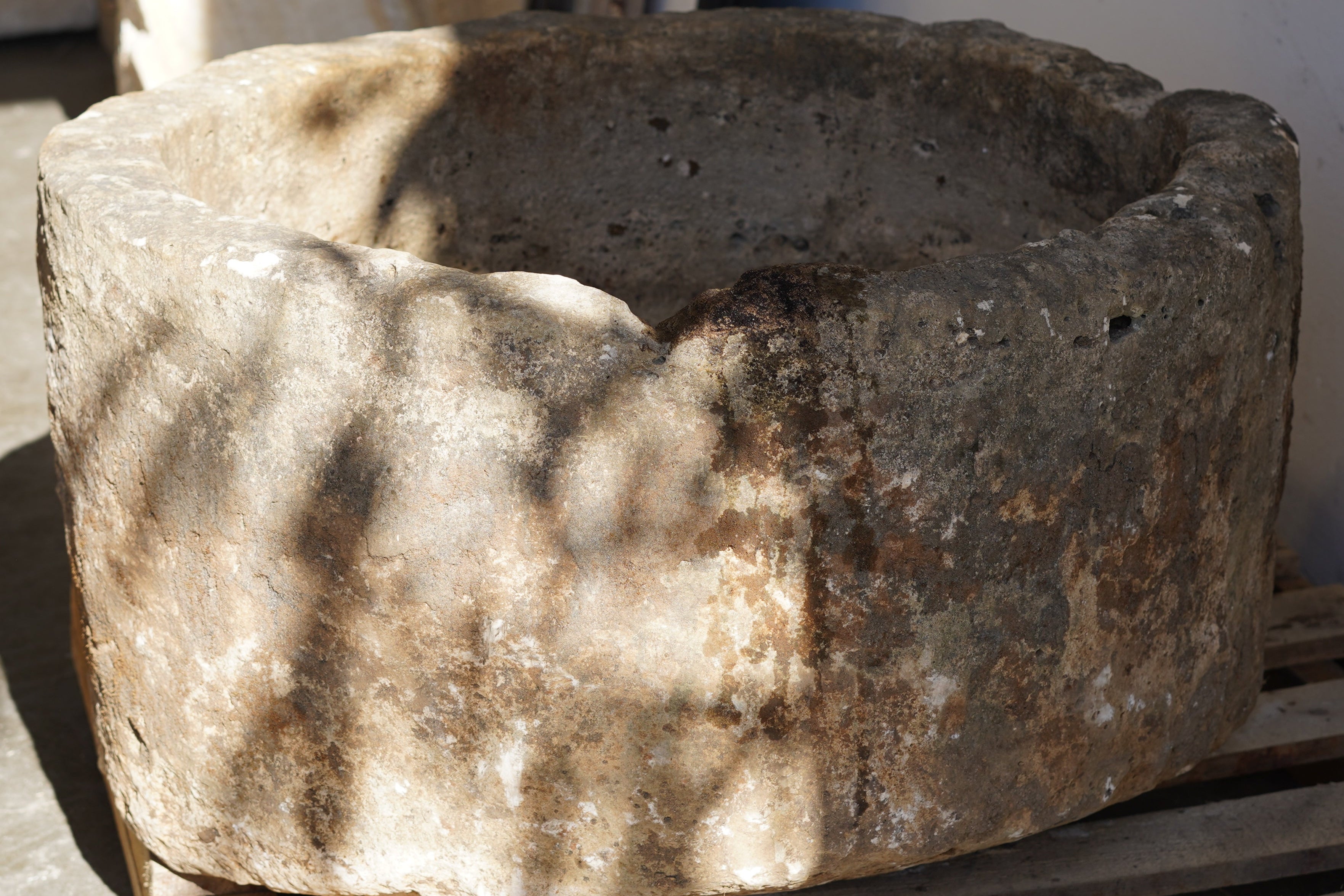 Close up of Antique Round Hand-Carved limestone with natural patina and aging over decades. Dimensions: 17" H x 33" W. partial sunlight and shadows cast from trees outside.