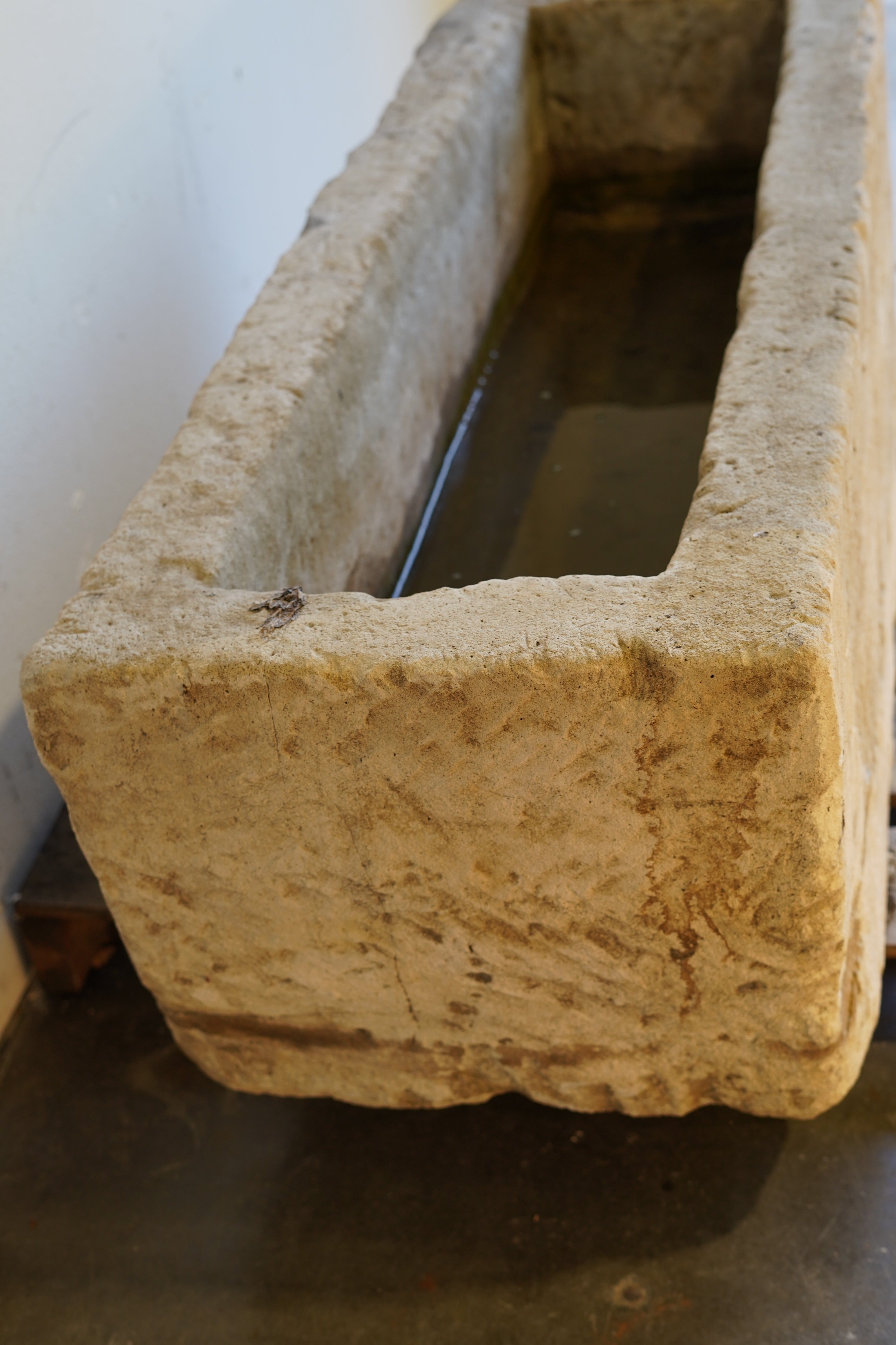 Side angle of antique limestone planter positioned against a white garage backdrop