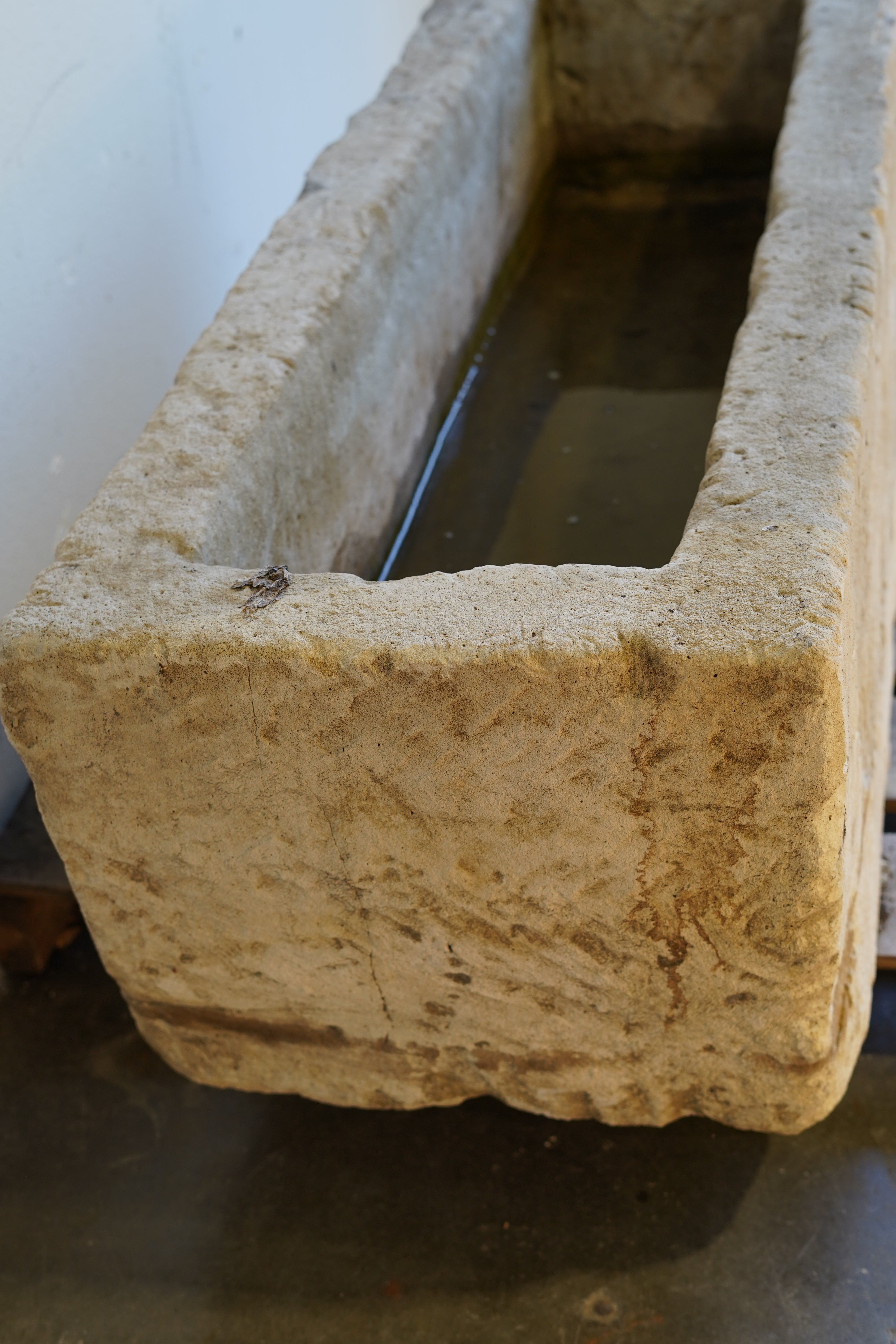 Side angle of antique limestone planter positioned against a white garage backdrop