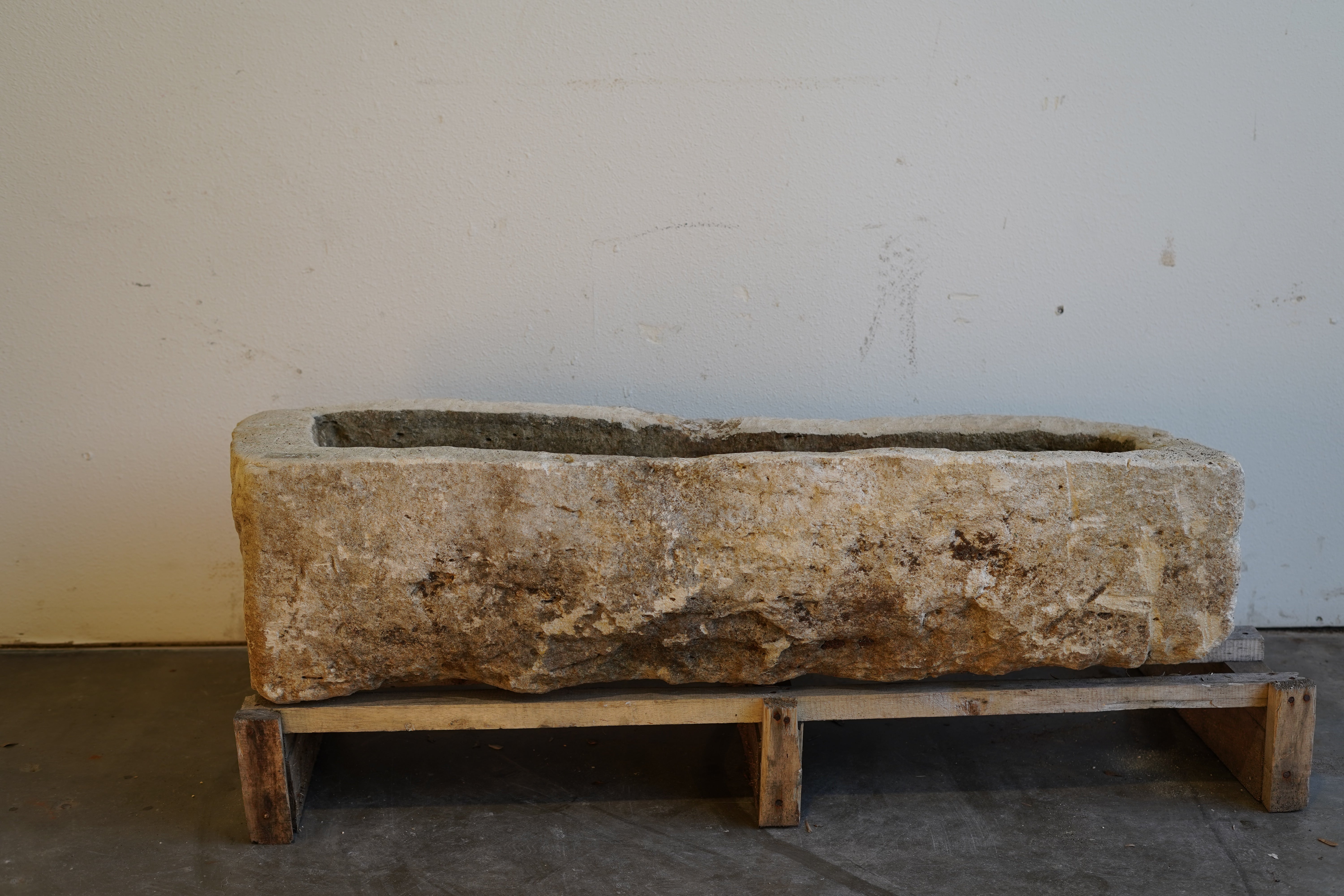 Rustic stone trough planter with visible wear and chisel marks, front-facing view in natural light